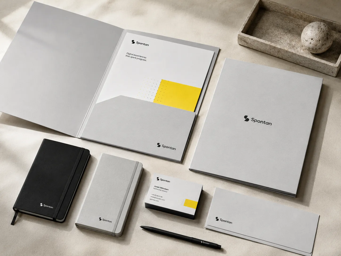 A Spontan presentation folder open with its printed insert, beside notebooks, business cards and a pen