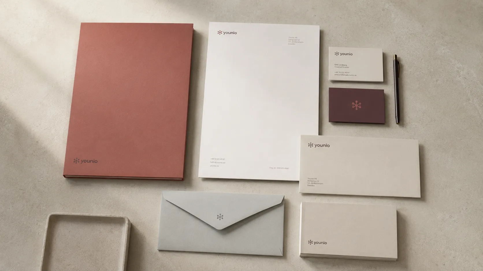 Younio stationery laid out flat: terracotta folder, letterhead, business cards in cream and aubergine, envelopes and a compliment slip