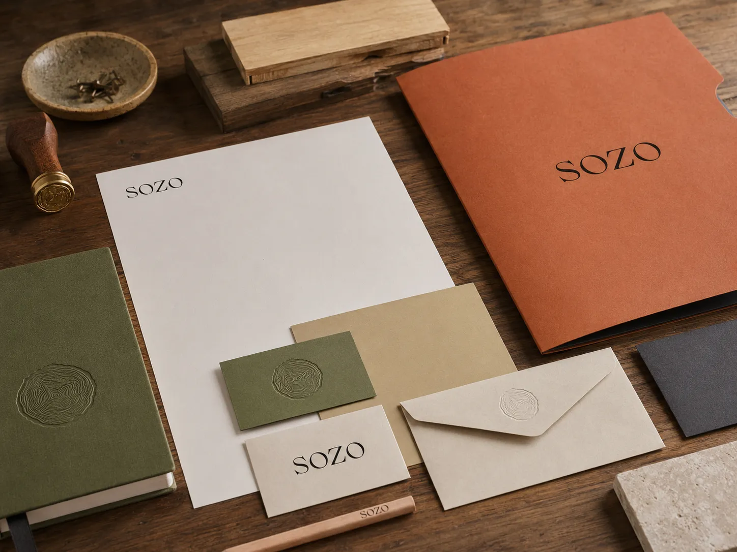 SOZO stationery on dark wood: embossed notebook, letterhead, cards, terracotta folder, wax-sealed envelope and brass stamp